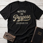 Made on Purpose t-shirt in Black — Ephesians 2:10 Christian tee flat lay with Holy Bible and ichthys on whitewashed wood