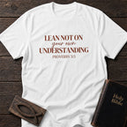 Lean Not on Your Own Understanding t-shirt in White — Proverbs 3:5 Christian tee flat lay with Holy Bible and ichthys on dark wood