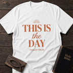 This Is the Day t-shirt in White — Psalm 118:24 Christian tee flat lay with Holy Bible and ichthys on dark wood