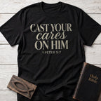 Cast Your Cares on Him t-shirt in Black — 1 Peter 5:7 Christian tee flat lay with Holy Bible and ichthys on whitewashed wood