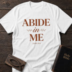 Abide in Me t-shirt in White — John 15:4 Christian tee flat lay with Holy Bible and ichthys on dark wood