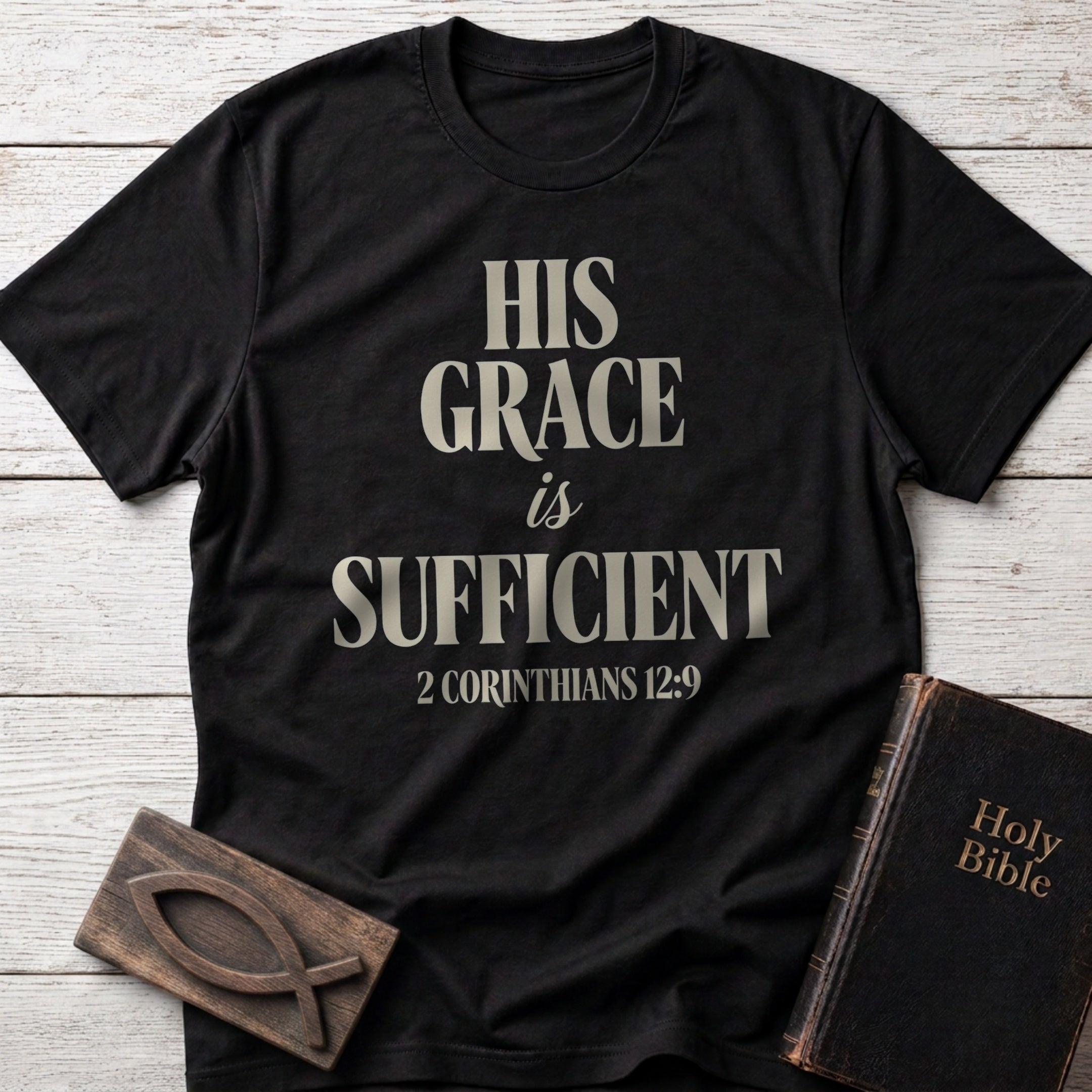 His Grace Is Sufficient t-shirt in Black — 2 Corinthians 12:9 Christian tee flat lay with Holy Bible and ichthys on whitewashed wood