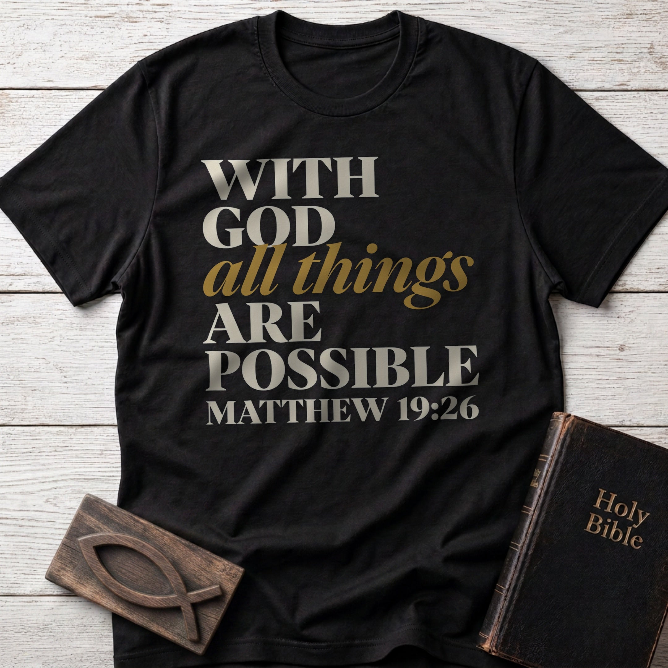 With God All Things Are Possible t-shirt in Black — Matthew 19:26 Christian tee flat lay with Holy Bible and ichthys on whitewashed wood