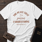 The Peace That Passes Understanding t-shirt in White — Philippians 4:7 Christian tee flat lay with Holy Bible and ichthys on dark wood