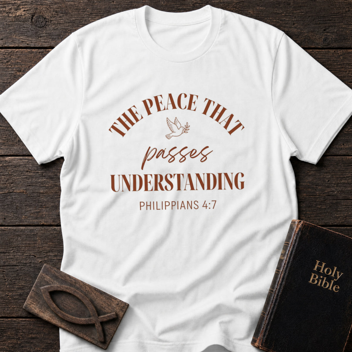 The Peace That Passes Understanding t-shirt in White — Philippians 4:7 Christian tee flat lay with Holy Bible and ichthys on dark wood