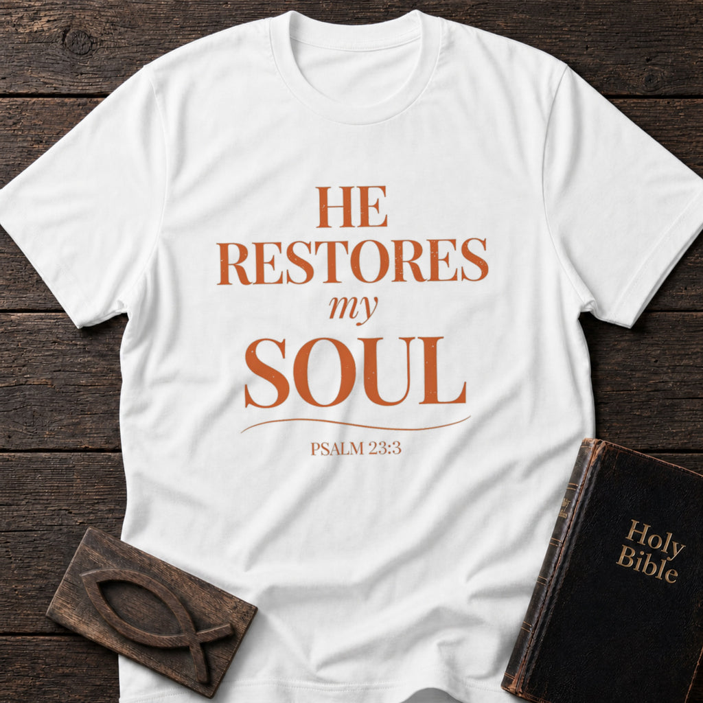 He Restores My Soul t-shirt in White — Psalm 23:3 Christian tee flat lay with Holy Bible and ichthys on dark wood
