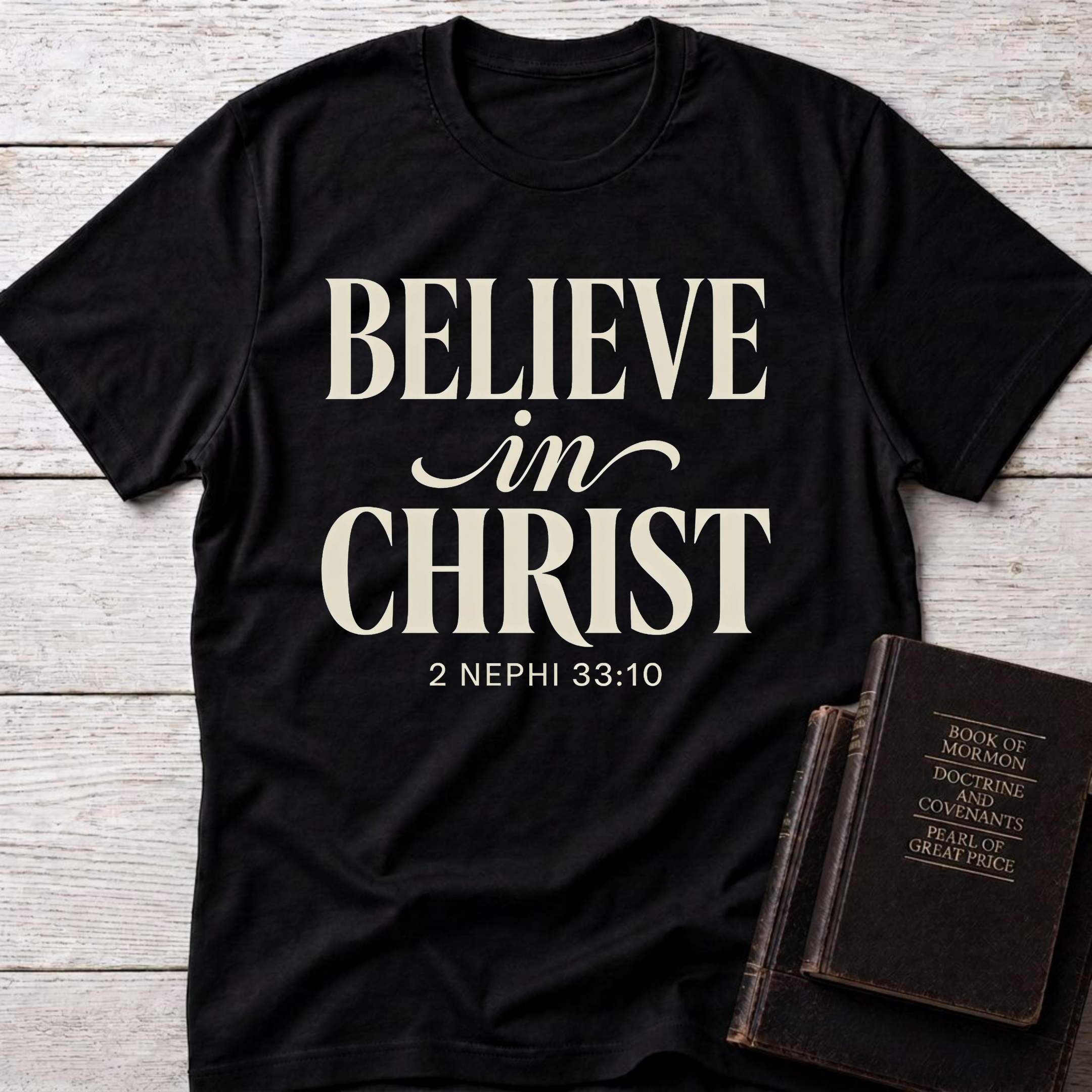 Believe in Christ t-shirt in black — 2 Nephi 33:10 Christian tee flat lay with Holy Bible and ichthys on dark wood