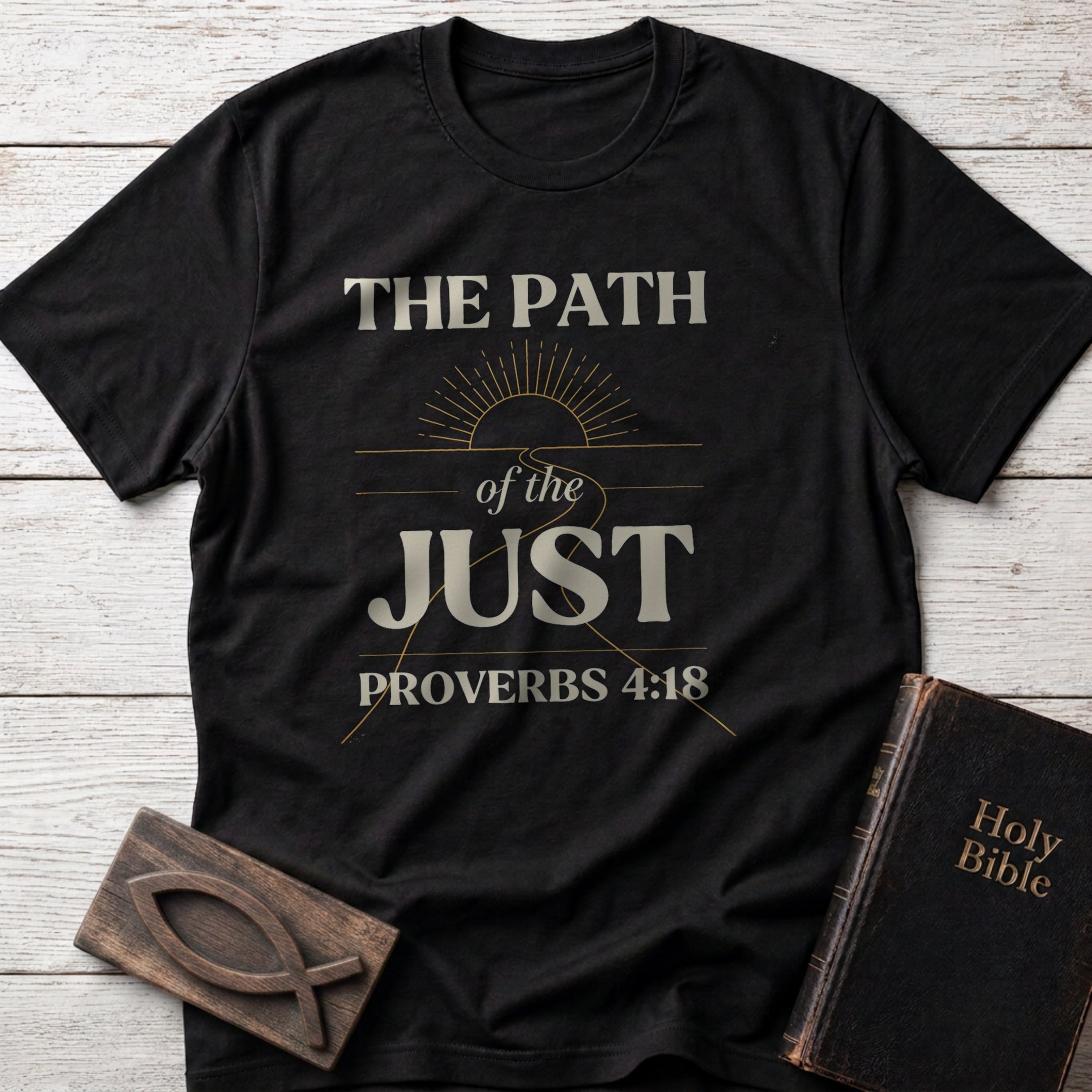 The Path of the Just t-shirt in Black — Proverbs 4:18 Christian tee flat lay with Holy Bible and ichthys on whitewashed wood