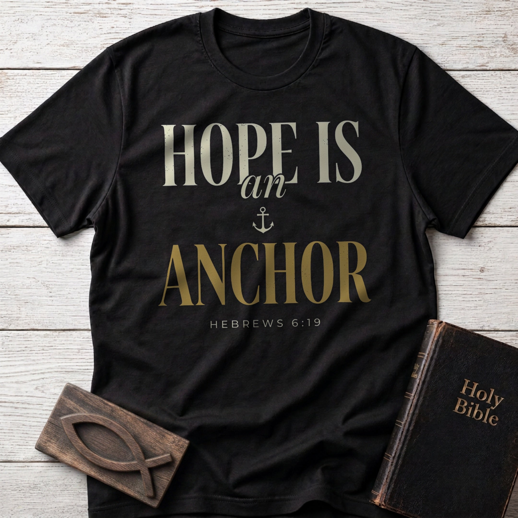 Hope Is an Anchor t-shirt in Black — Hebrews 6:19 Christian tee flat lay with Holy Bible and ichthys on whitewashed wood