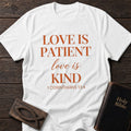 Love Is Patient, Love Is Kind t-shirt in White — 1 Corinthians 13:4 Christian tee flat lay with Holy Bible and ichthys on dark wood