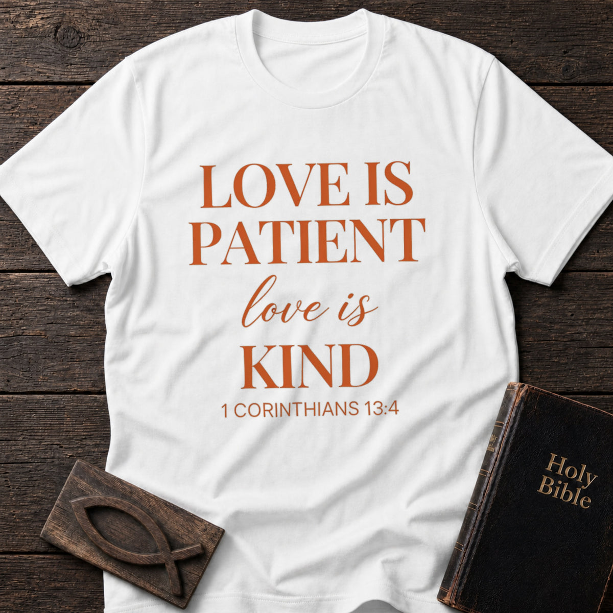 Love Is Patient, Love Is Kind t-shirt in White — 1 Corinthians 13:4 Christian tee flat lay with Holy Bible and ichthys on dark wood