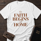 Faith Begins at Home t-shirt in White — Christian tee flat lay with Holy Bible and ichthys on dark wood