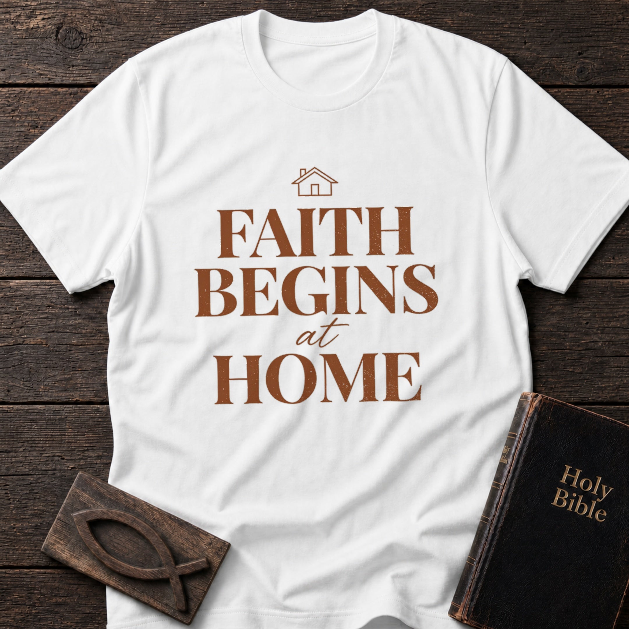 Faith Begins at Home t-shirt in White — Christian tee flat lay with Holy Bible and ichthys on dark wood