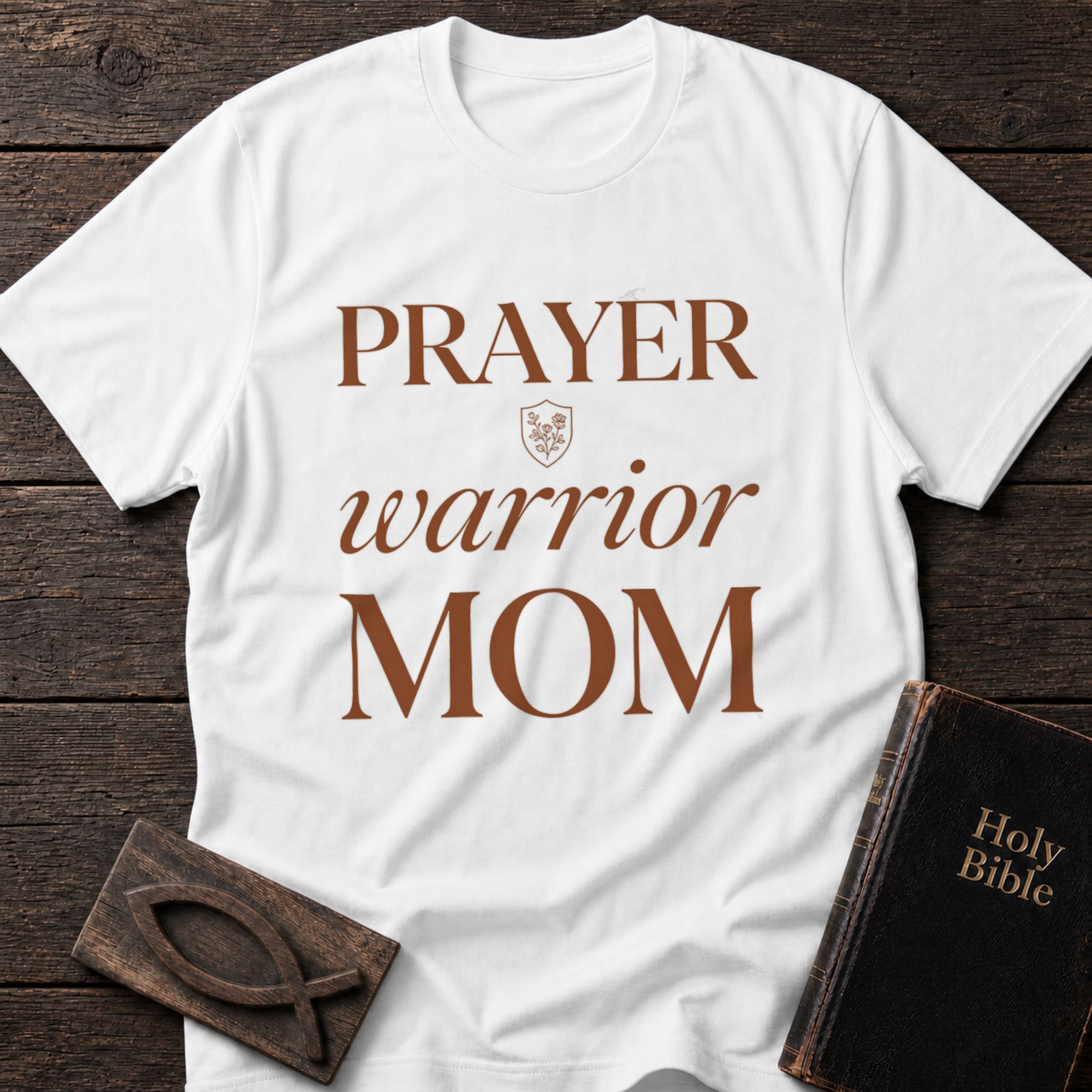 Prayer Warrior Mom t-shirt in White — Christian tee flat lay with Holy Bible and ichthys on dark wood
