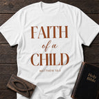 Faith of a Child t-shirt in White — Matthew 18:3 Christian tee flat lay with Holy Bible and ichthys on dark wood