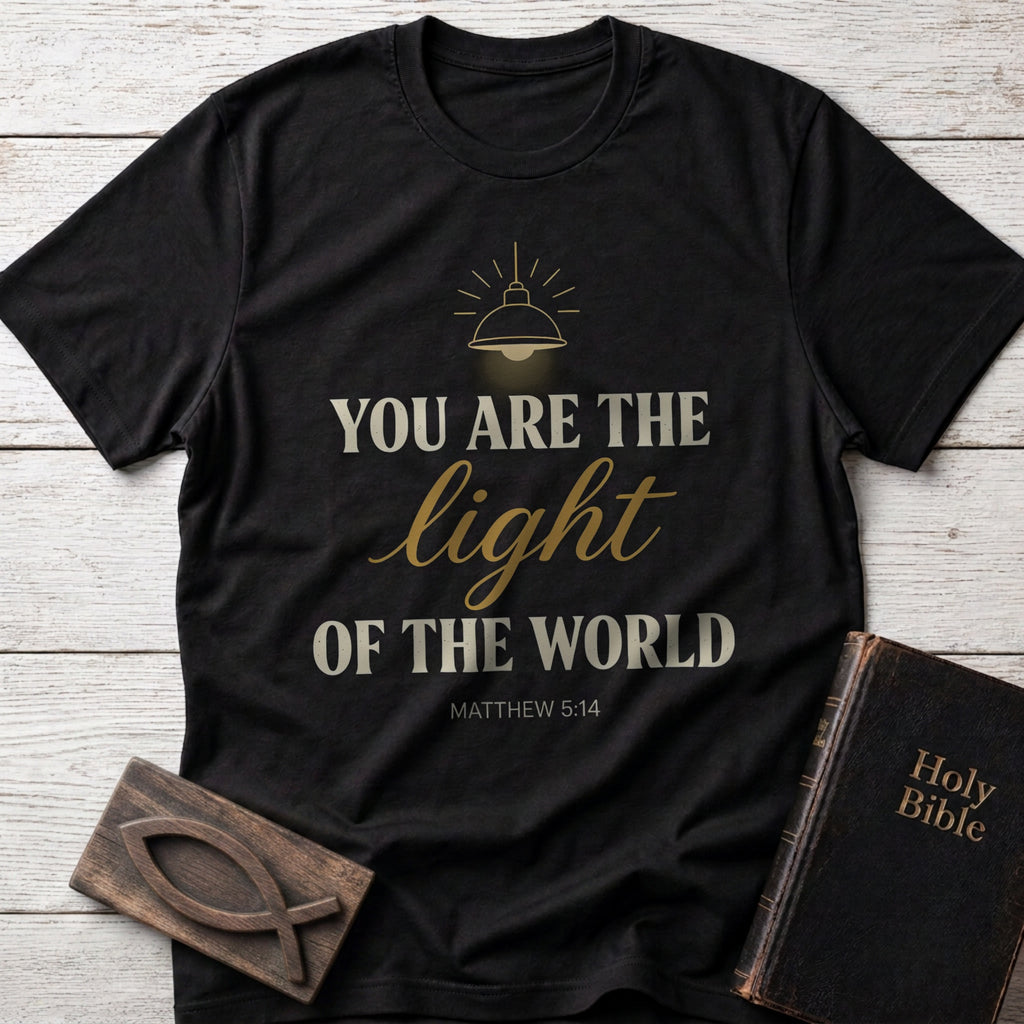 You Are the Light of the World t-shirt in Black — Matthew 5:14 Christian tee flat lay with Holy Bible and ichthys on whitewashed wood