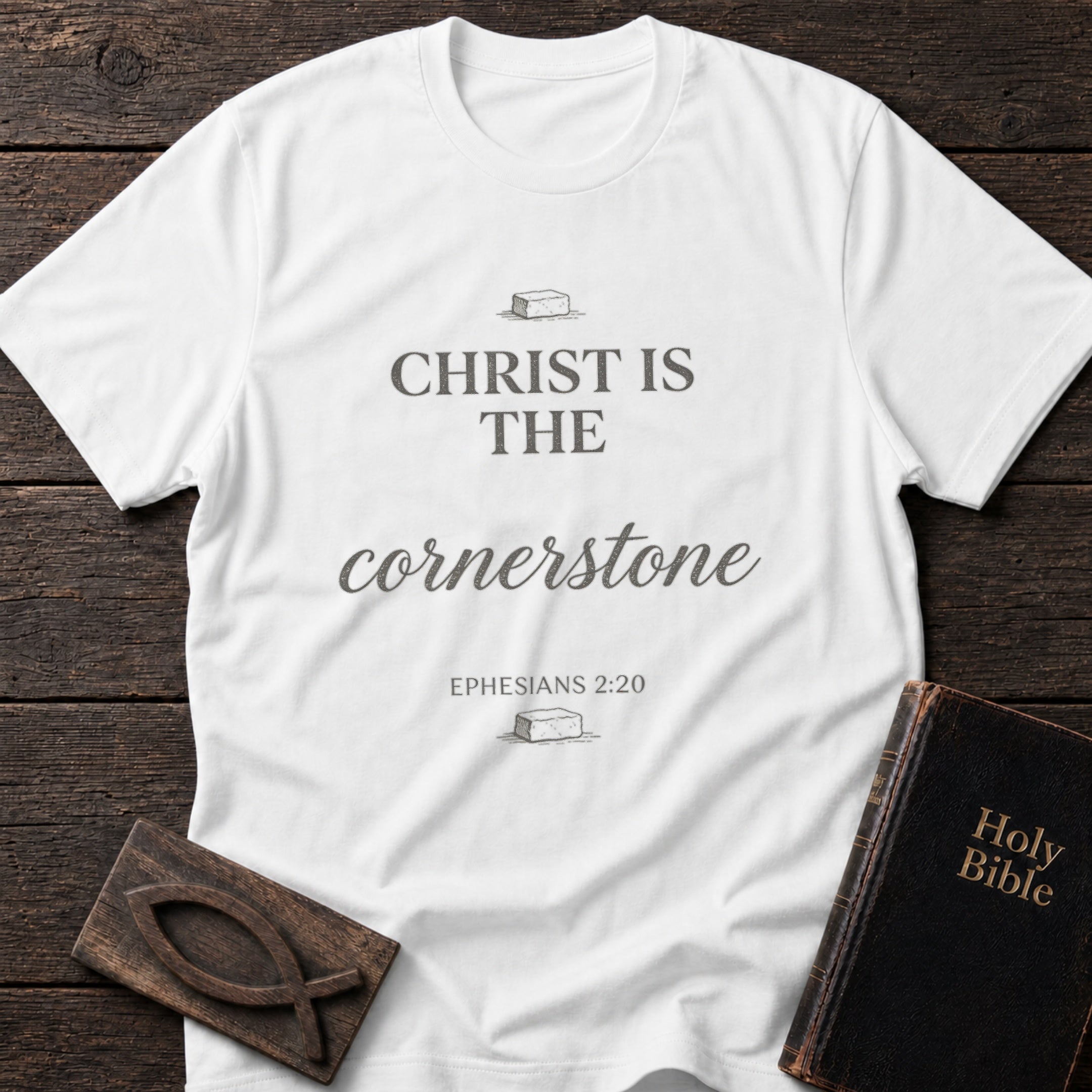 Christ Is the Cornerstone t-shirt in White — Ephesians 2:20 Christian tee flat lay with Holy Bible and ichthys on dark wood
