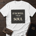 It Is Well With My Soul t-shirt in White — Christian tee flat lay with Holy Bible and ichthys on dark wood