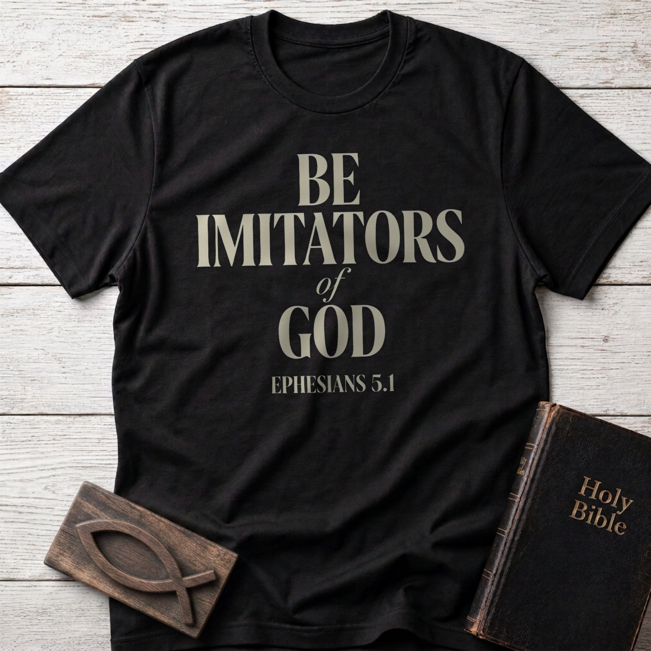 Be Imitators of God t-shirt in Black — Ephesians 5:1 Christian tee flat lay with Holy Bible and ichthys on whitewashed wood