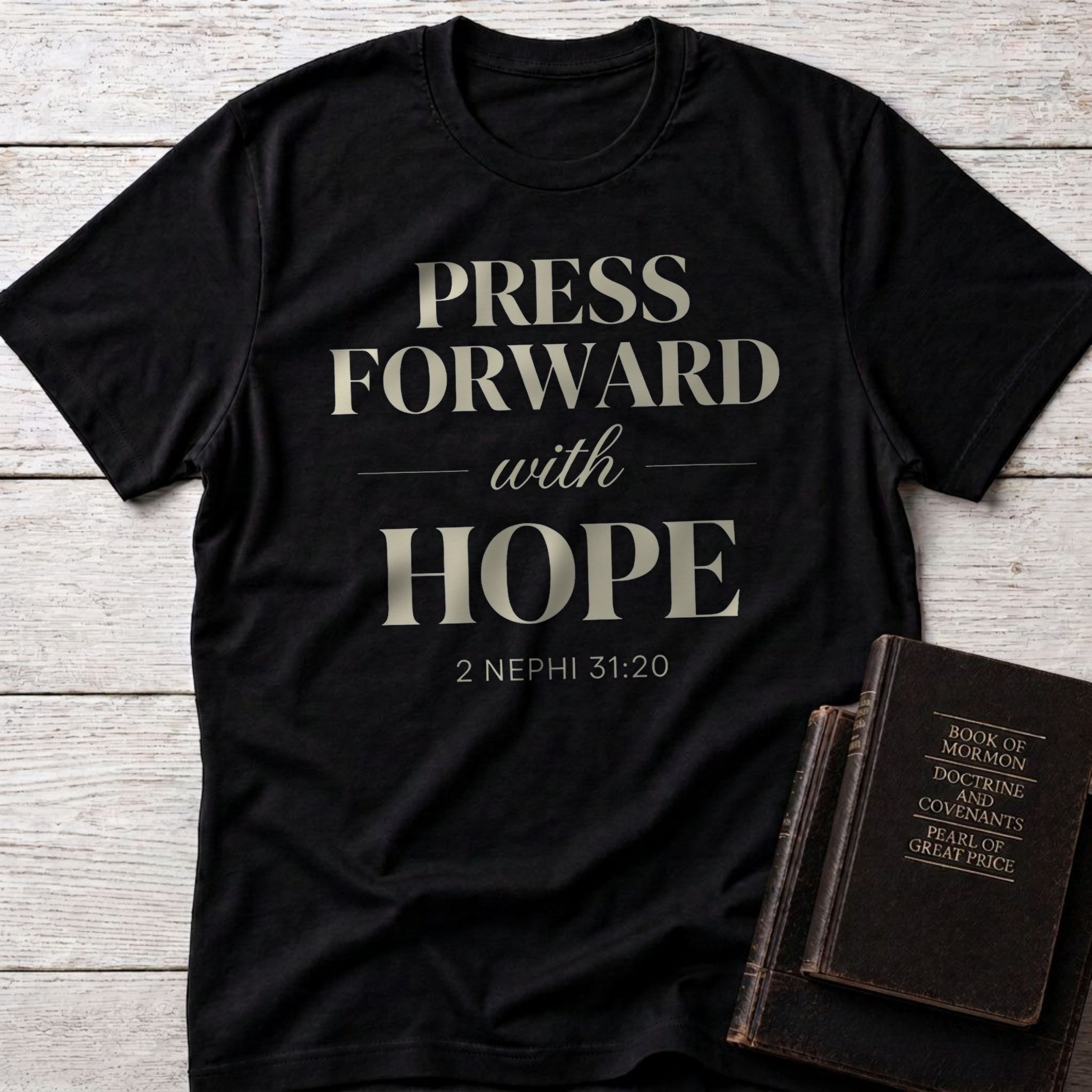 Press Forward with Hope t-shirt in Black — 2 Nephi 31:20 Christian tee flat lay with Book of Mormon scripture set on whitewashed wood