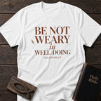 Be Not Weary in Well-Doing t-shirt in White — Galatians 6:9 Christian tee flat lay with Holy Bible and ichthys on dark wood