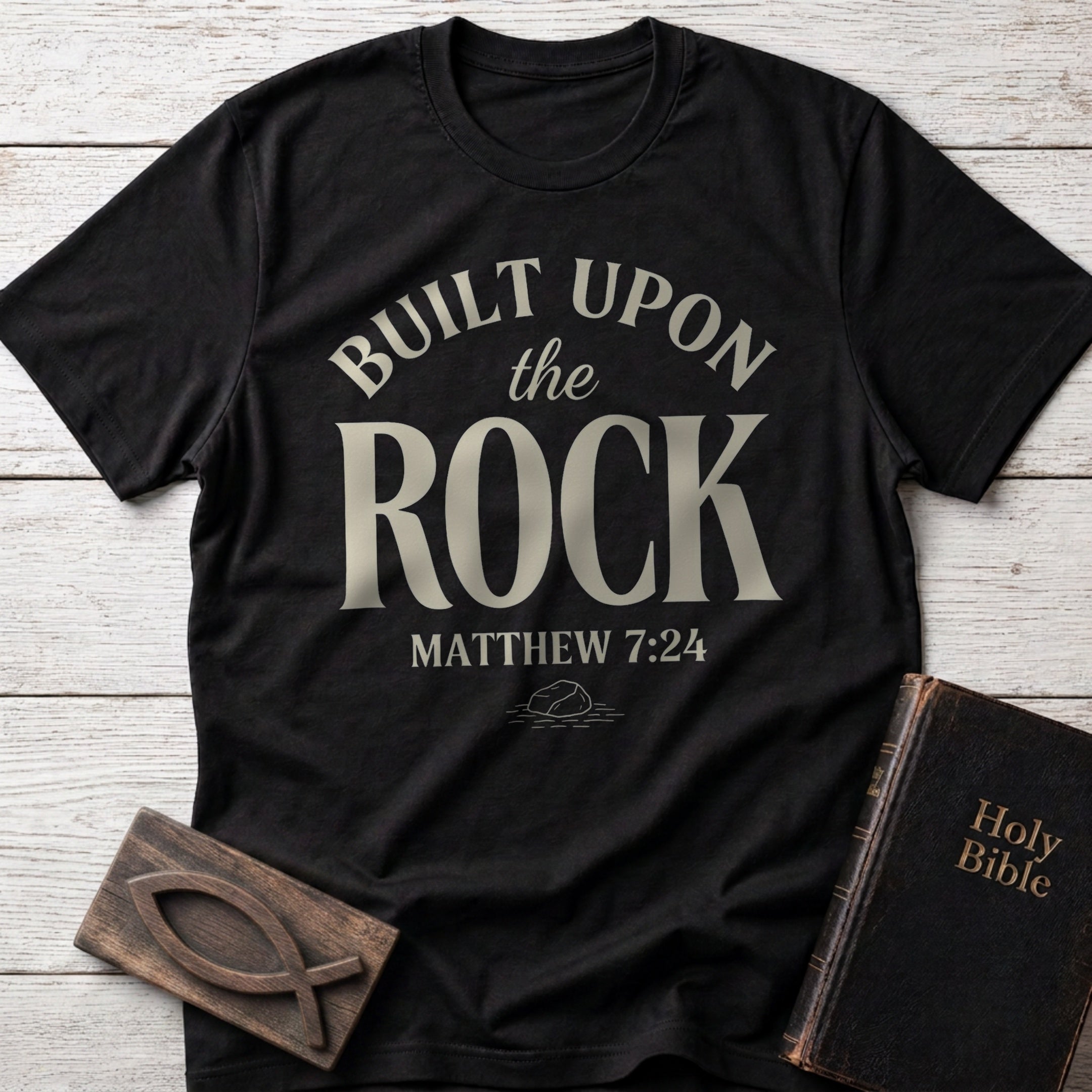 Built Upon the Rock t-shirt in Black — Matthew 7:24 Christian tee flat lay with Holy Bible and ichthys on whitewashed wood
