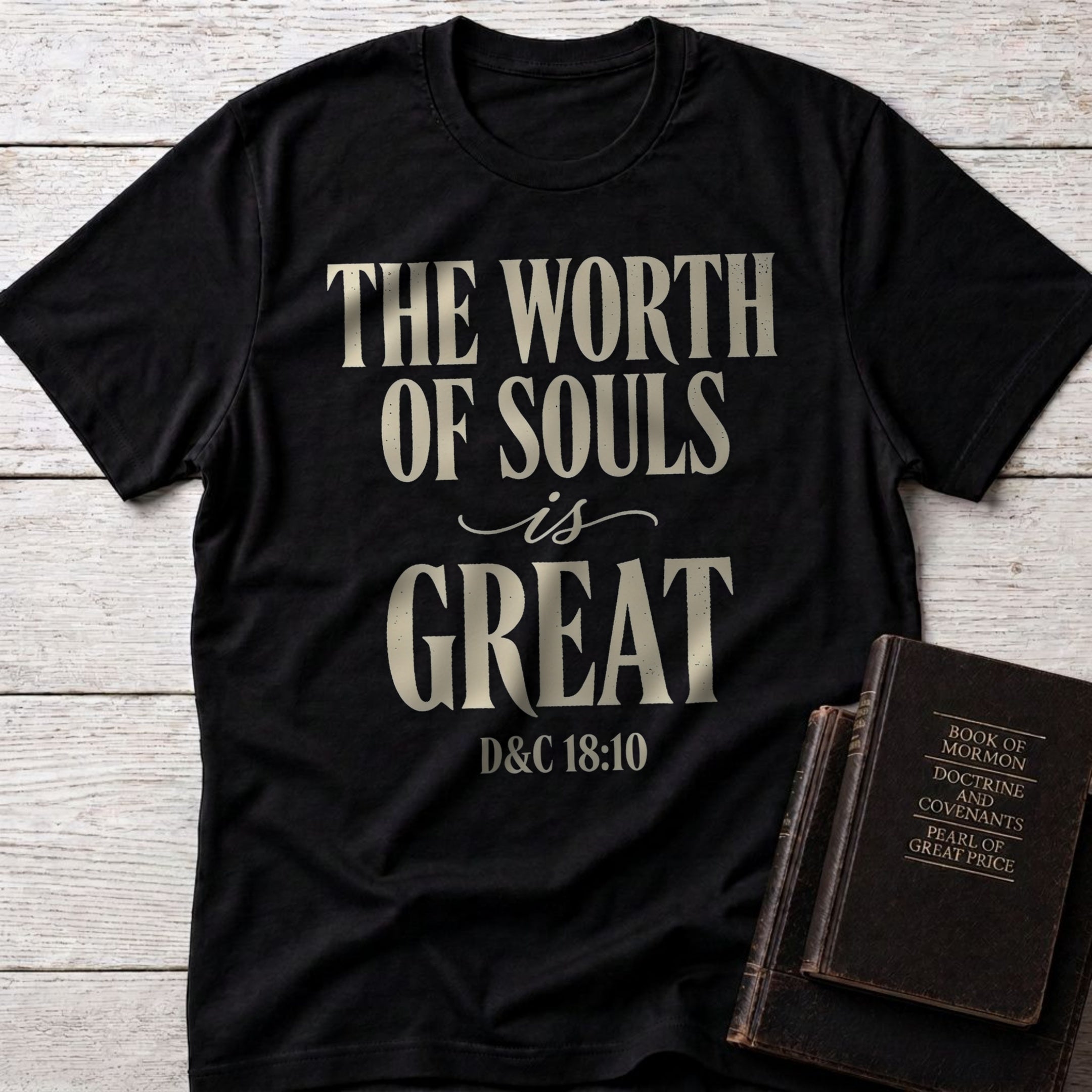 The Worth of Souls Is Great t-shirt in Black — D&C 18:10 Christian tee flat lay with Book of Mormon scripture set on whitewashed wood