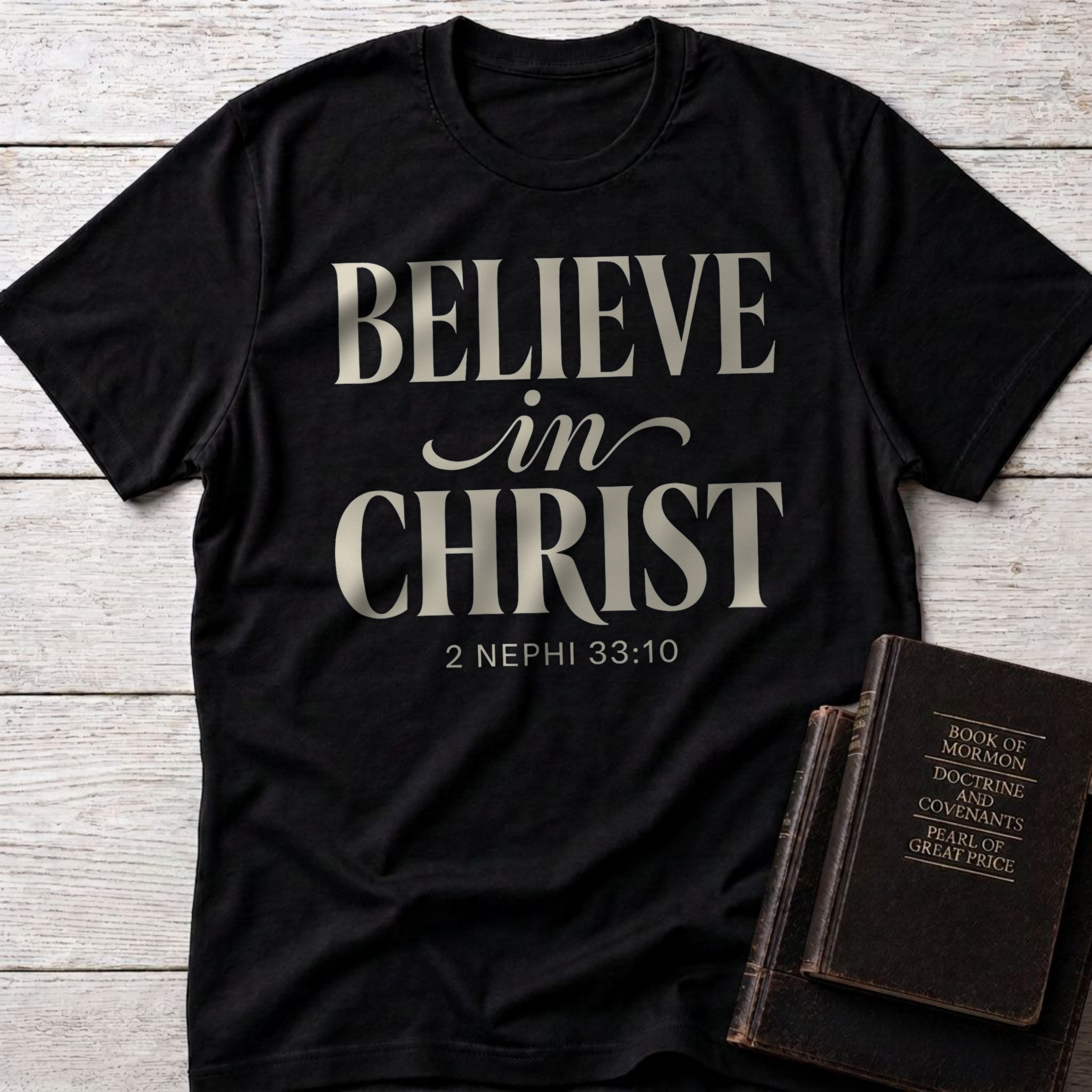 Believe in Christ t-shirt in Black — 2 Nephi 33:10 Christian tee flat lay with Book of Mormon scripture set on whitewashed wood