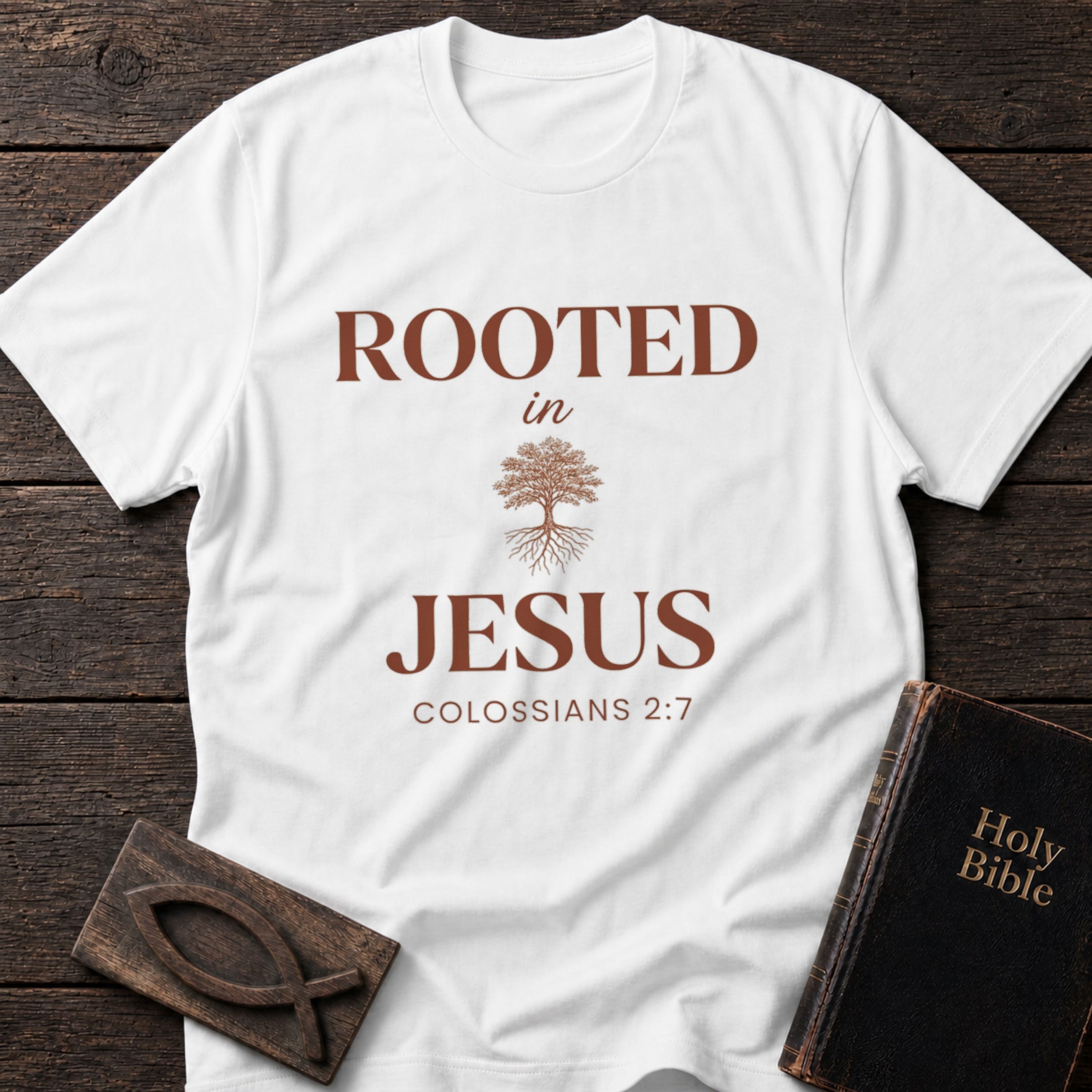 Rooted in Jesus t-shirt in White — Colossians 2:7 Christian tee flat lay with Holy Bible and ichthys on dark wood