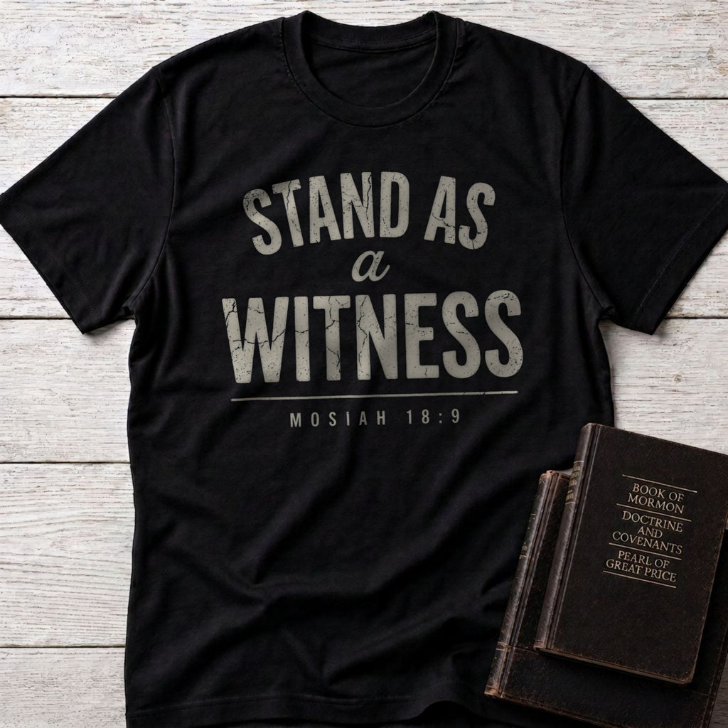 Stand as a Witness t-shirt in Black — Mosiah 18:9 Christian tee flat lay with scripture books on whitewashed wood