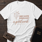 She Hath Wrought a Good Work t-shirt in White — Mark 14:6 Christian tee flat lay with Holy Bible and ichthys on dark wood