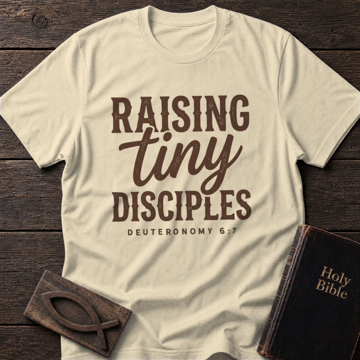 Raising Tiny Disciples t-shirt in Natural — motherhood Christian tee flat lay with Holy Bible and ichthys on dark wood